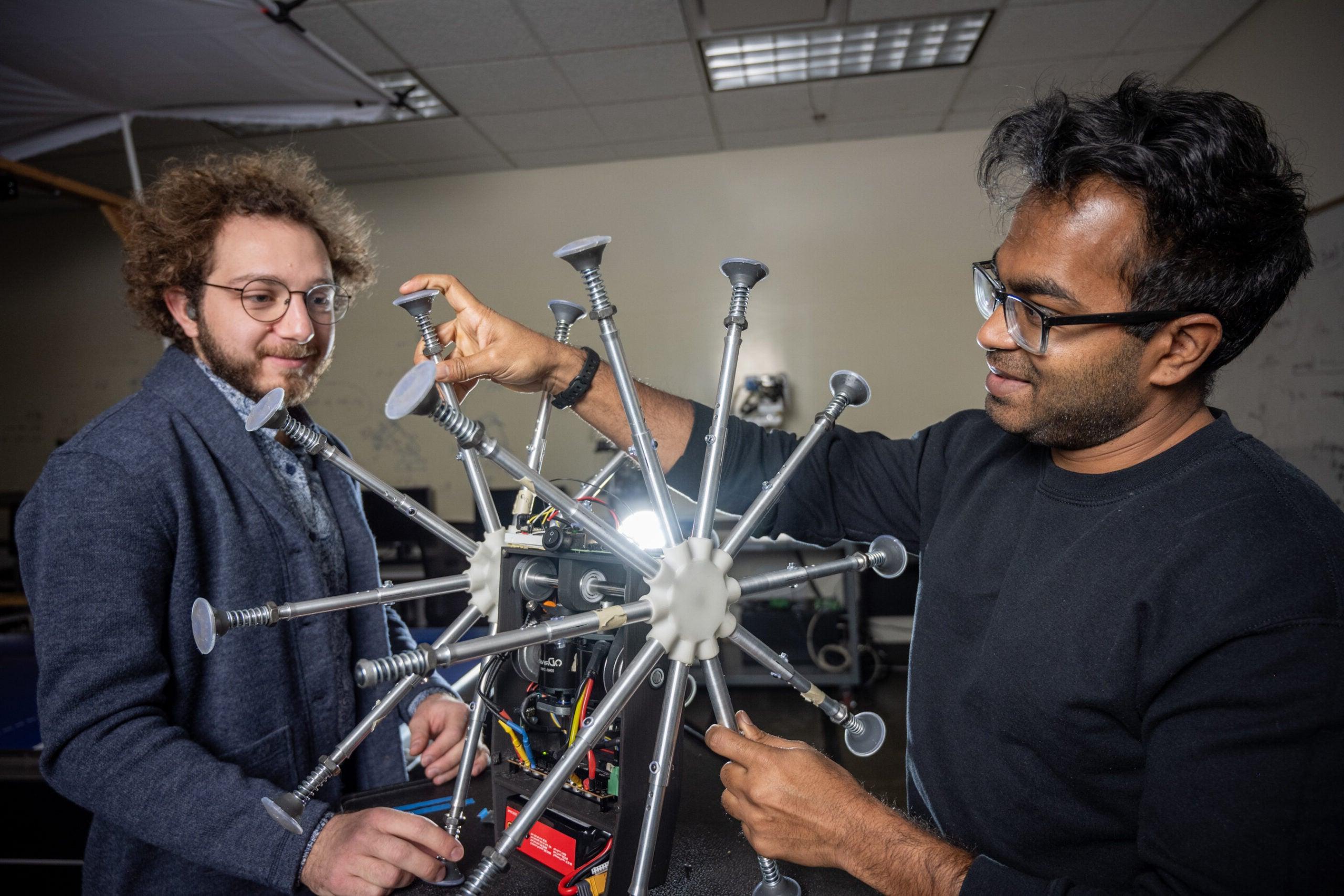 Two graduate students in the Mechanical and Biomedical Engineering program examine a robot in the Robot Control Lab.